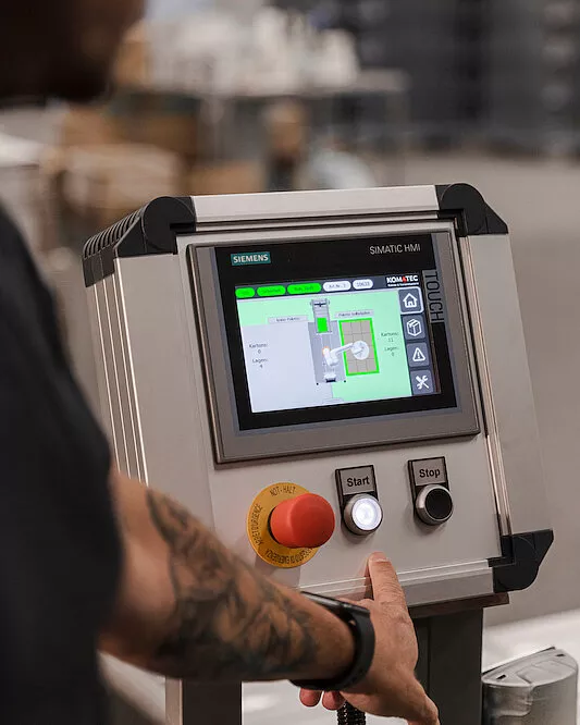 Eine Person bedient ein industrielles Siemens SIMATIC HMI-Touchscreen-Bedienfeld mit sichtbaren Start- und Stopptasten.